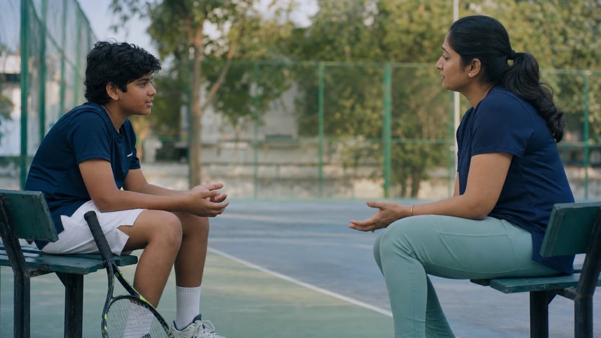 A junior player speaking with a listening parent at the same eye level beside an empty tennis court.